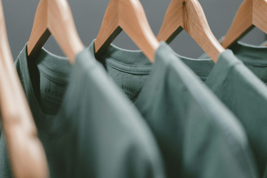 Green T-shirts aligned on wooden hangers